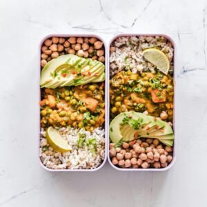 Delicious vegan lunchboxes featuring chickpeas, rice, avocado, and curry on a white background.